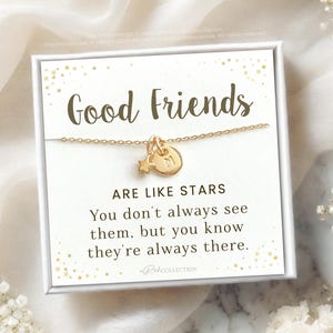 May include: A white card with gold glitter and the text "Good Friends Are Like Stars You don't always see them, but you know they're always there."  RekCOLLECTION is printed at the bottom of the card. A gold necklace with a star and a letter charm is displayed on the card.