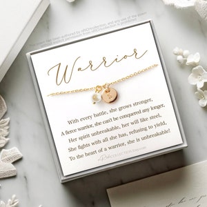 May include: A gold necklace with a small pearl charm and a round disc charm with the letter "S" on it. The necklace is in a white box with a poem that reads "Warrior" and "With every battle, she grows stronger, A fierce warrior, she can't be conquered any longer, Her spirit unbreakable, her will like steel, She fights with all she has, refusing to yield, To the heart of a warrior, she is unbreakable!"