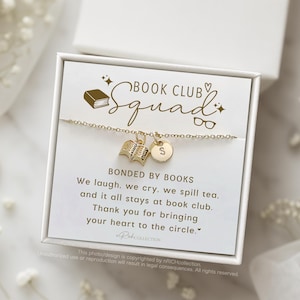 May include: A white box with a gold charm bracelet featuring a book charm and a letter charm. The box has a gold inscription that reads "Book Club Squad" and "Bonded by Books". The inscription continues with the text "We laugh, we cry, we spill tea, and it all stays at book club. Thank you for bringing your heart to the circle."