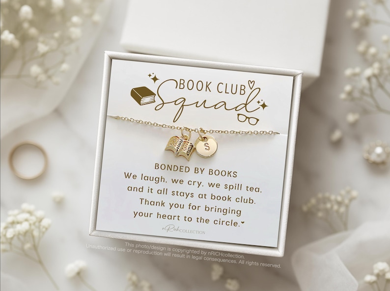 May include: A white box with a gold charm bracelet featuring a book charm and a letter charm. The box has a gold inscription that reads "Book Club Squad" and "Bonded by Books". The inscription continues with the text "We laugh, we cry, we spill tea, and it all stays at book club. Thank you for bringing your heart to the circle."
