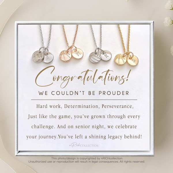 May include: A white card with the text "Congratulations! We couldn't be prouder" and a message about hard work, determination, and perseverance. The card features four necklaces with small charms, each with a different letter.