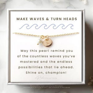 May include: A gold necklace with a pearl and a gold charm that says "S". The necklace is in a white box with the text "MAKE WAVES & TURN HEADS" and a message about the pearl reminding you of the countless waves you've mastered and the endless possibilities that lie ahead. The message ends with "Shine on, champion!"