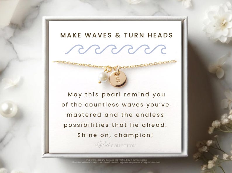 May include: A gold necklace with a pearl and a gold charm that says "S". The necklace is in a white box with the text "MAKE WAVES & TURN HEADS" and a message about the pearl reminding you of the countless waves you've mastered and the endless possibilities that lie ahead. The message ends with "Shine on, champion!"