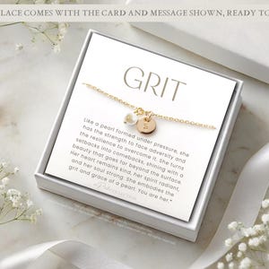 Op de afbeelding: Een witte cadeaudoos met een gouden ketting en een kaart met de tekst "GRIT" en een boodschap over de kracht en veerkracht van een parel.