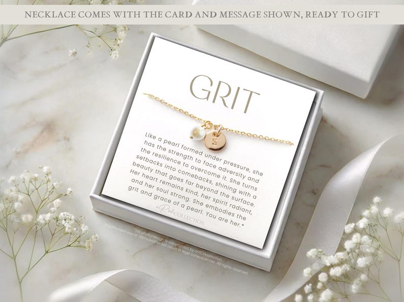 Op de afbeelding: Een witte cadeaudoos met een gouden ketting en een kaart met de tekst "GRIT" en een boodschap over de kracht en veerkracht van een parel.