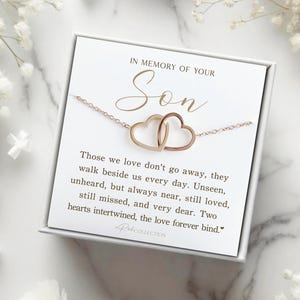 May include: A white card with the text "In memory of your Son" and a quote about love and loss. The card is in a white box with a rose gold necklace with two intertwined hearts.