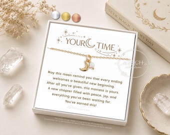 Könnte beinhalten: Eine goldfarbene Halskette mit einem kleinen Mondsichel-Anhänger und einer winzigen weißen Perle, präsentiert in einer weißen Geschenkbox. Die Box enthält den Text "YOUR TIME" und eine inspirierende Botschaft über Neuanfänge.