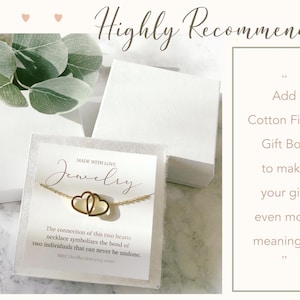 May include: A gold necklace with two interlocking hearts on a white card with the text "Made with Love Jewelry" and a description of the necklace. The card is in a white gift box. The text "Add Cotton Filled Gift Box to make your gift even more meaningful" is in a white box with a gray border.