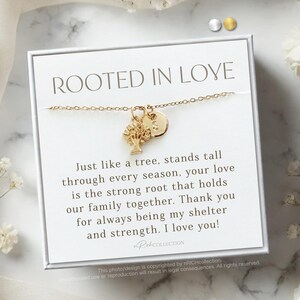 May include: A white card with the text "Rooted in Love" and a quote about family and love. The card features a gold necklace with a tree charm and a small circle charm.
