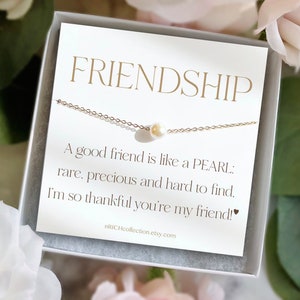 Może przedstawiać: Biała kartka z pozłacanymi napisami zawiera tekst "FRIENDSHIP" i "A good friend is like a PEARL: rare, precious and hard to find. I'm so thankful you're my friend!" Złoty łańcuszek z pojedynczą perłą zwisa nad tekstem. Kartka znajduje się w białym pudełku.