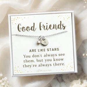 May include: A silver necklace with a star charm and a letter 'A' charm. The necklace is displayed on a white card with gold glitter and the text "Good Friends Are Like Stars You don't always see them, but you know they're always there."