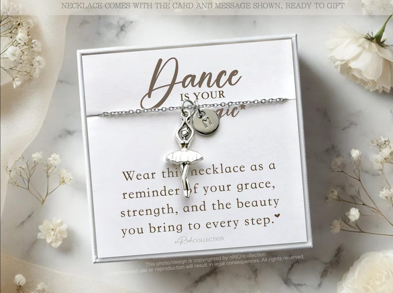 May include: A white card with a silver necklace featuring a ballerina charm and a letter charm. The card reads "Dance is your magic" and includes a message about grace, strength, and beauty.