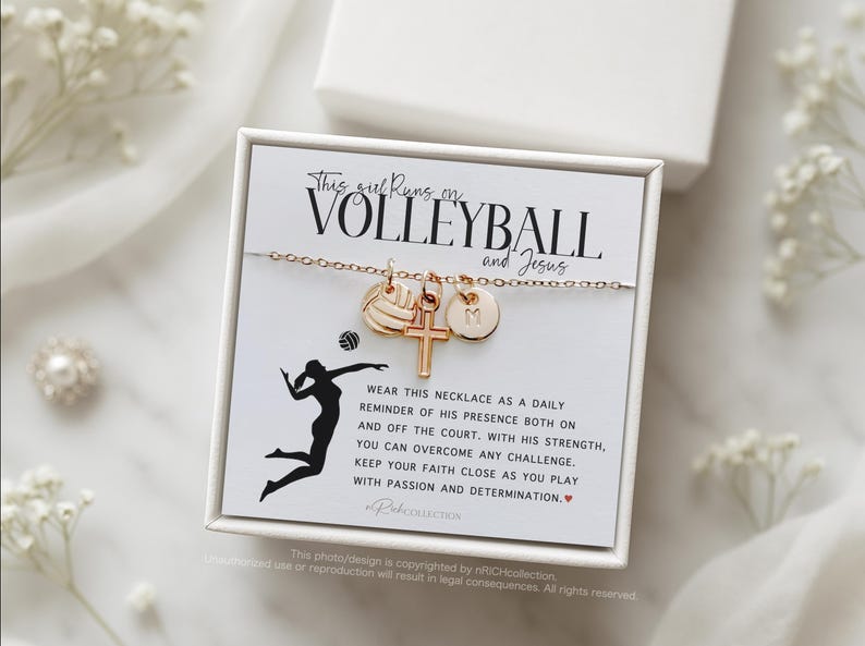 May include: A white box with a gold necklace inside. The necklace has a volleyball charm, a cross charm, and a letter charm. The box has a message that says "This girl runs on volleyball and Jesus".