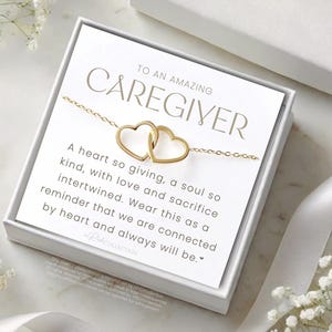 May include: A white gift box with a gold necklace inside. The box has a message that reads "To an amazing caregiver. A heart so giving, a soul so kind, with love and sacrifice intertwined. Wear this as a reminder that we are connected by heart and always will be."