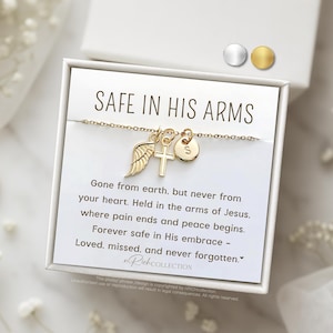 May include: A gold necklace with a cross, angel wing, and initial charm in a white box with the text "SAFE IN HIS ARMS" and a message about being held in the arms of Jesus.