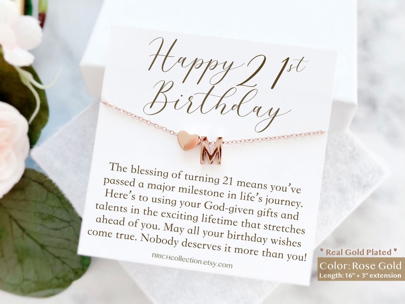 May include: A card with the text "Happy 21st Birthday" and a rose gold necklace with a heart charm and a letter "M" charm. The card includes a message about turning 21 and the necklace is 16 inches long with a 3 inch extension.
