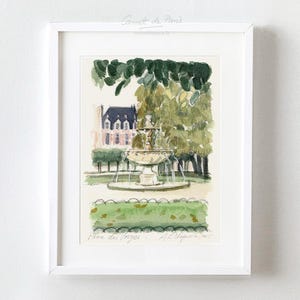 May include: A framed watercolor print of a park scene. The artwork depicts a fountain, trees, and a building. The print is in a white frame and features the text "Carnet de Paris" and "Parc des Vosges".