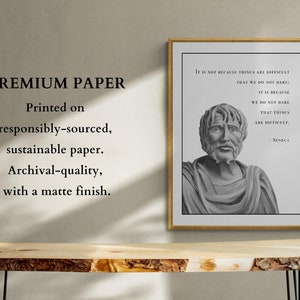 May include: A framed print with a black and white image of a man's bust. The print has a quote by Seneca: "It is not because things are difficult that we do not dare; it is because we do not dare that things are difficult." The print is on a wooden table with a light wood grain.