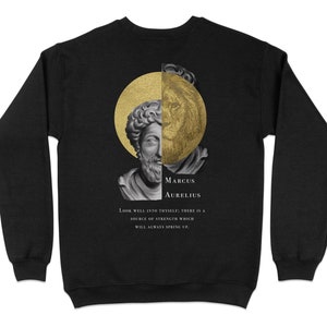 Op de afbeelding: Zwart sweatshirt met een gouden en witte afbeelding van Marcus Aurelius, een Romeinse keizer en filosoof, met een citaat van hem: "Kijk goed in jezelf; er is een bron van kracht die altijd zal opwellen."