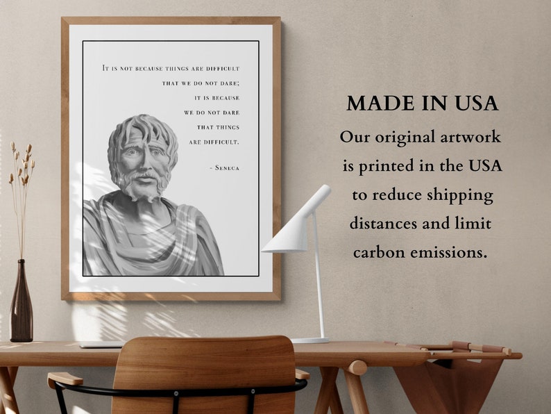 May include: A black and white print of a bust of Seneca the Younger with a quote about courage. The quote reads "It is not because things are difficult that we do not dare: It is because we do not dare that things are difficult." The print is framed and hanging on a wall. The text "MADE IN USA" is printed below the image. The text below "MADE IN USA" reads "Our original artwork is printed in the USA to reduce shipping distances and limit carbon emissions."