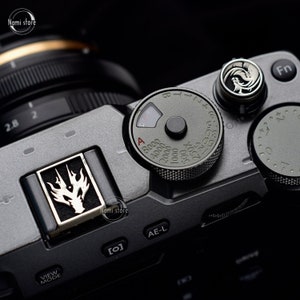 May include: A close-up of a gray camera with a black lens. The camera has a black dial with white numbers and a black button in the center. The dial is labeled with the letters "A" and "B" and the numbers "8000", "4000", "2000", "1000", "500", "250", "125", "60", "30", "15", "8", "4", "2", "1", and "1/2". The camera also has a black button labeled "Fn" and a black button labeled "AE-L".