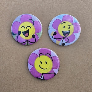 May include: Three round buttons featuring a cartoon flower design. Each button has a yellow center with a smiling face and purple petals. The buttons have black outlines and are set against a neutral background.