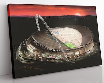 Op de afbeelding: Een luchtfoto van een groot, modern stadion met een intrekbaar dak. Het stadion is 's nachts verlicht en de lucht is helderrood en oranje. Het stadion is omgeven door een donker, grasbegroeid gebied.