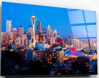 May include: A vibrant cityscape at dusk, featuring the iconic Space Needle and illuminated skyscrapers. The image captures the city's skyline against a deep blue sky, with a mountain visible in the distance. The artwork is a print on a glossy surface.