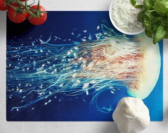 May include: A blue cutting board with a jellyfish design. The board is surrounded by various kitchen ingredients, including tomatoes, garlic, basil, and a bowl of white sauce.