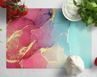 Peut inclure: Une planche à découper colorée avec un motif abstrait rose, violet et bleu avec des accents dorés. La planche est en verre et a une surface lisse.