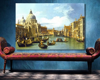 Op de afbeelding: Een ingelijste canvas print van een Venetiaanse kanaalscène, met boten, gebouwen en een koepelkerk. De print wordt weergegeven boven een rode chaise longue met sierlijke details en donkere houten poten, tegen een blauwe muur.