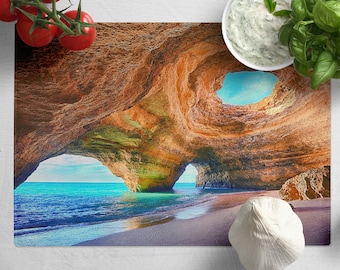 Peut inclure: Une planche à découper en verre colorée avec une photographie d'une grotte marine avec une mer bleue et une plage de sable.