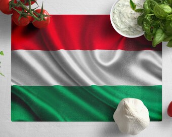 May include: A white cutting board with a red, white, and green Hungarian flag printed on it. There are fresh tomatoes, basil, garlic, and a bowl of white sauce on the board.