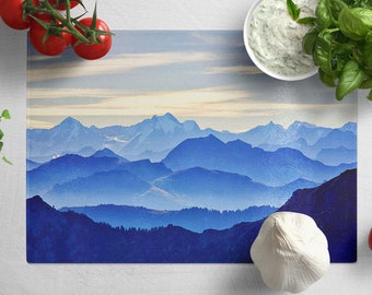 May include: A blue and white glass cutting board with a mountain range design. The board is on a white surface with a bowl of dip, tomatoes, and herbs.