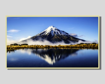 May include: A snow-capped mountain reflected in a still lake. The mountain is surrounded by a light mist and the sky is a clear blue.