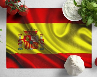 May include: A red and yellow Spanish flag with the national coat of arms in the center. The flag is surrounded by fresh ingredients, including tomatoes, garlic, basil, and a bowl of white sauce.