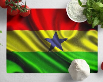 May include: A red, yellow, and green flag with a black star in the center. The flag is on a white surface with a bowl of dip, a head of garlic, and tomatoes.