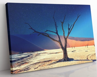 Op de afbeelding: Een eenzame, dode boom staat in een woestijnlandschap onder een sterrenhemel. De zandduinen zijn fel oranje en de lucht is diepblauw.