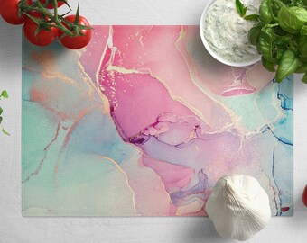 Peut inclure: Une planche à découper en verre avec un motif marbré rose, bleu et or. La planche est lisse et brillante.