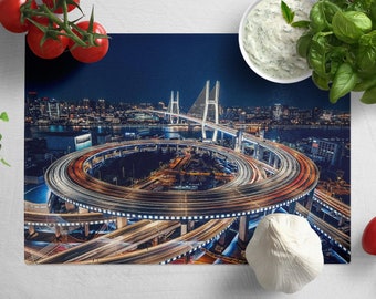 May include: A rectangular placemat featuring a nighttime cityscape with a bridge and a complex highway interchange. The image has long exposure light trails. Fresh tomatoes, basil, and a bowl of dip surround the placemat.