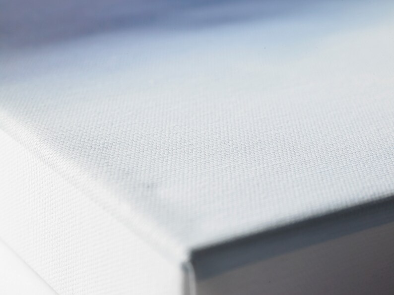 May include: Close-up of a white canvas surface with a fine, even texture. The canvas is stretched tightly over a frame, creating a smooth, flat surface.