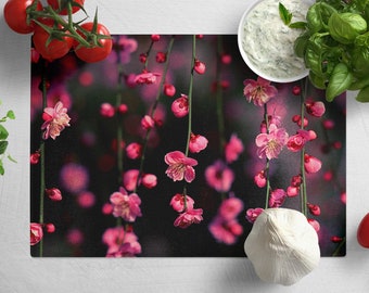 Peut inclure: Une planche à découper noire avec un motif floral composé de fleurs roses et de tiges vertes. La planche est entourée de divers ingrédients de cuisine, notamment des tomates, de l'ail et des herbes.