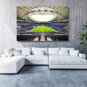 May include: A large, modern stadium with a retractable roof, viewed from the pitch level. The seats are purple and the pitch is green. The stadium is empty.