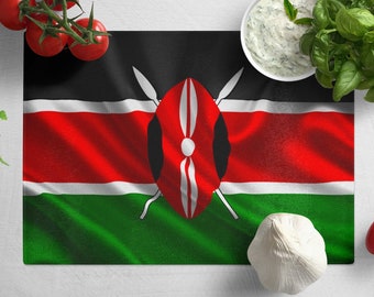 May include: A white cutting board with a Kenyan flag printed on it. The board is surrounded by fresh ingredients, including tomatoes, garlic, basil, and a bowl of white sauce.
