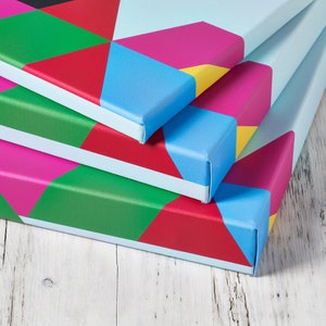 May include: Three colorful canvas prints with geometric patterns in shades of red, pink, blue, green, and yellow. The prints are stacked on top of each other, with the top print slightly offset from the bottom two.