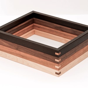 May include: Four wooden picture frames stacked on top of each other. The frames are made of different types of wood, including dark brown, light brown, and natural wood. The frames are all the same size and shape, and they are all joined together with a mitered joint.