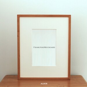 May include: A natural wood picture frame with a white mat and the text "FRAMEANDMATBOARD" printed on the mat. The frame is labeled "ALDER" at the bottom.