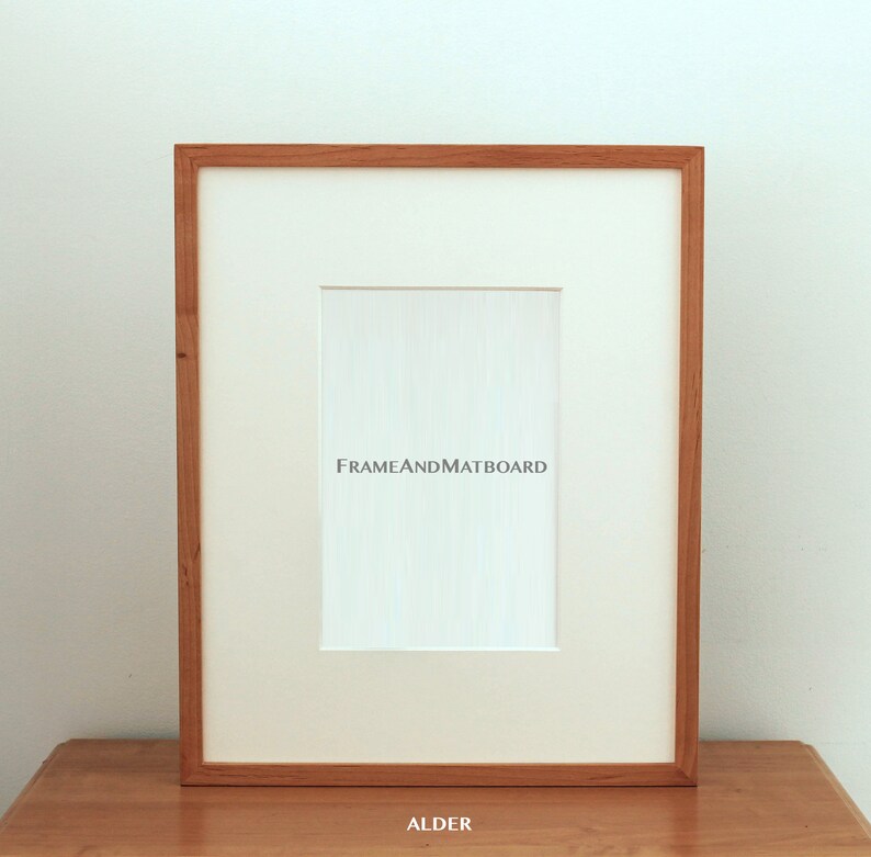 May include: A natural wood picture frame with a white mat and the text "FRAMEANDMATBOARD" printed on the mat. The frame is labeled "ALDER" at the bottom.