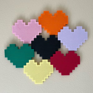 May include: Six heart-shaped wall decorations in different colours: pink, orange, purple, black, green, and yellow. Each heart is made of a textured material and has a pixelated design.