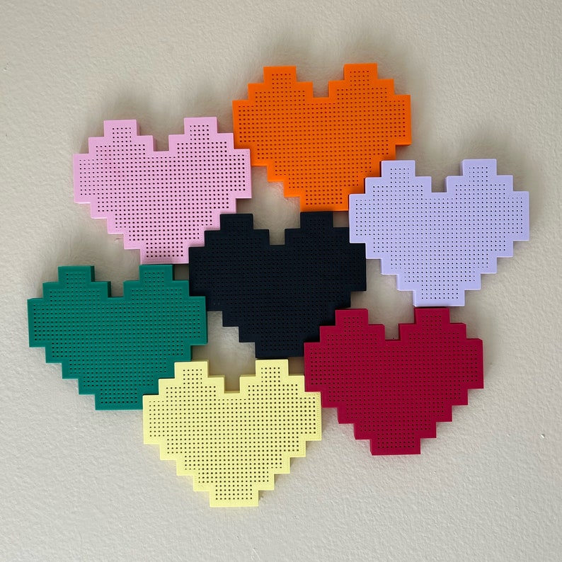 May include: Six heart-shaped wall decorations in different colours: pink, orange, purple, black, green, and yellow. Each heart is made of a textured material and has a pixelated design.
